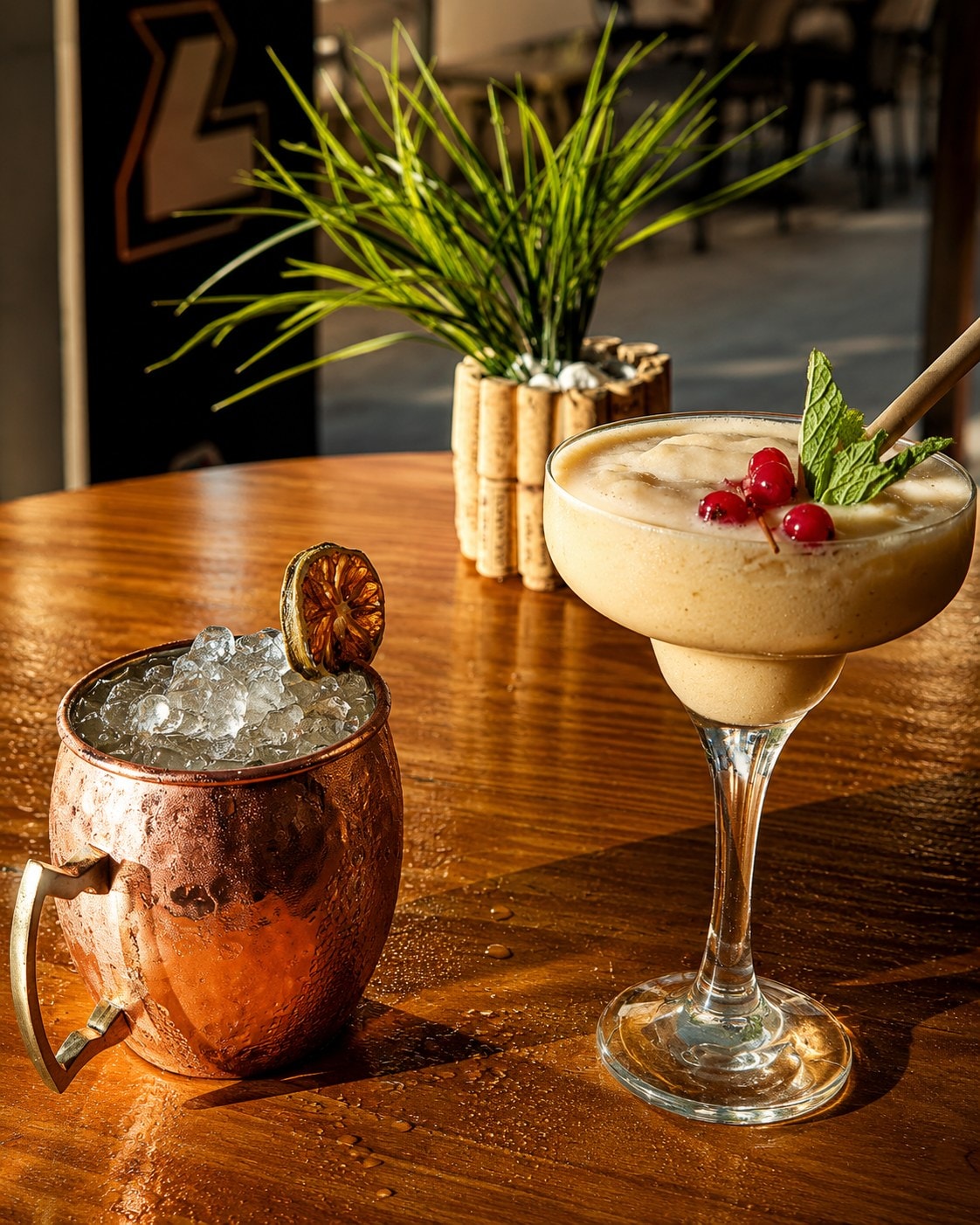 Cóctel en mug de cobre y copa de cristal con hielo y cítricos, a hora dorada.